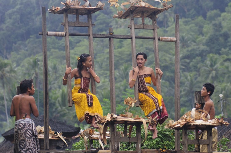Au village de Tenganan, de très anciennes traditions perdurent. Ici, deux jeunes filles conversent au cours d'un rite traditionnel, durant lequel les garçons inculquent le mouvement à la balancelle, symbolisant ainsi l'équilibre. (Crédit photo : www.andisucirta.com)